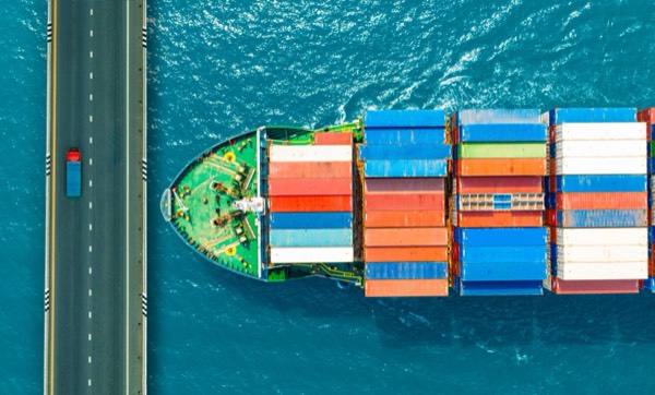 Containerschiff und Brücke mit Lastwagen aus der Luft